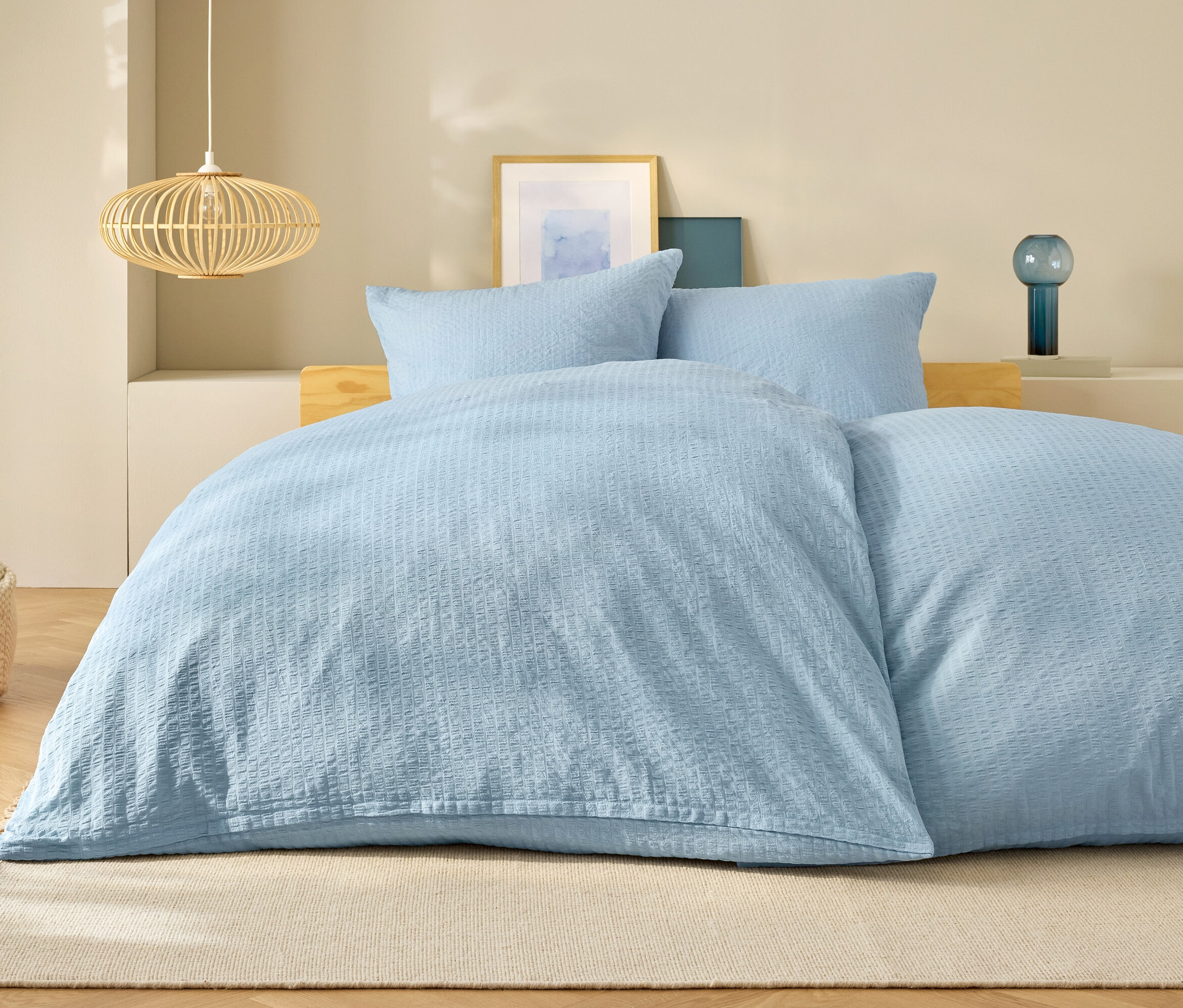 Világoskék ágynemű egy ágyon párnákkal és egy lámpával a háttérben.