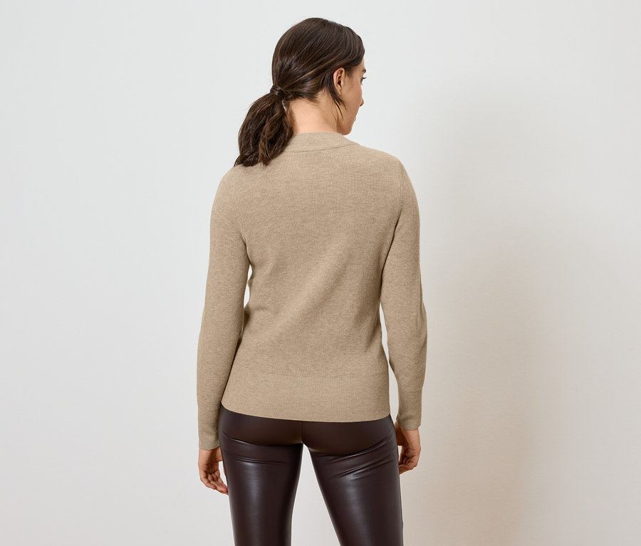 A fényképezőgépnek háttal álló nő bézs színű pulóvert és barna bőr nadrágot visel.