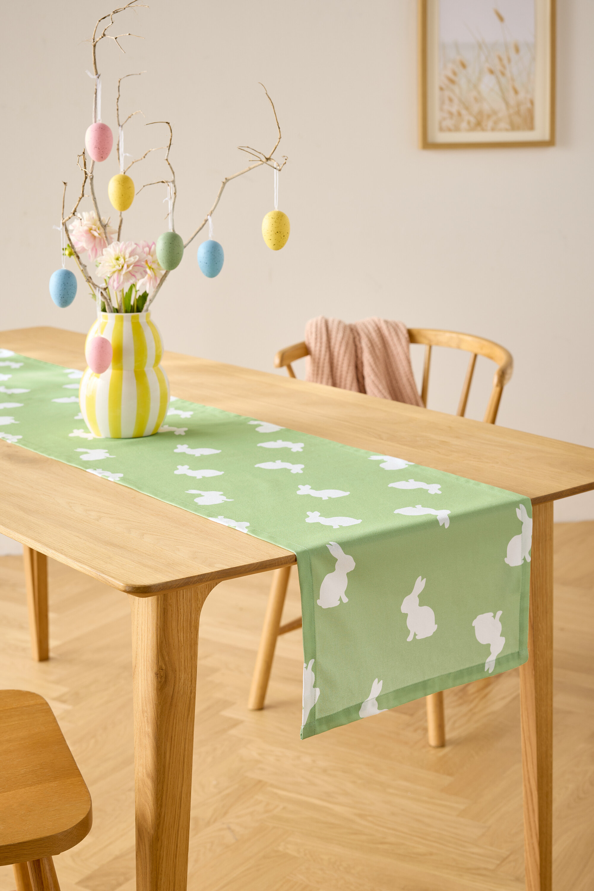 Ékezőasztal világoszöld, fehér nyuszi mintás asztali futóval, virágvázával és húsvéti tojás dekorációval.