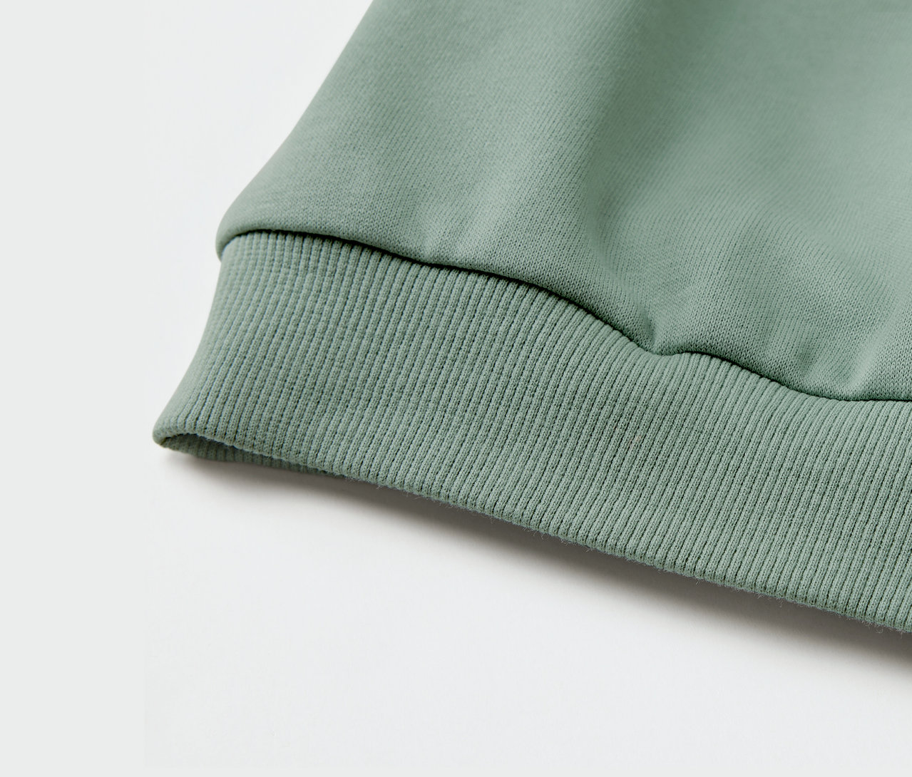 Egy zöld, passzés ujjú gyermek szabadidőfelső részletének fényképe.