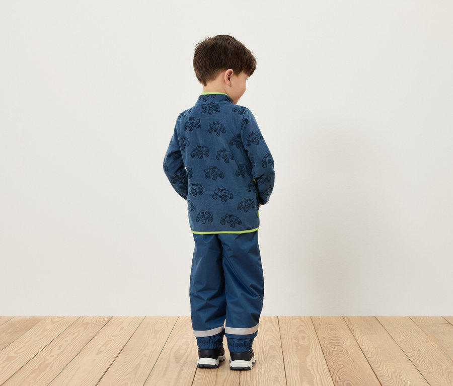 Egy fiú háttal áll, kék, autómintás ruhát visel.