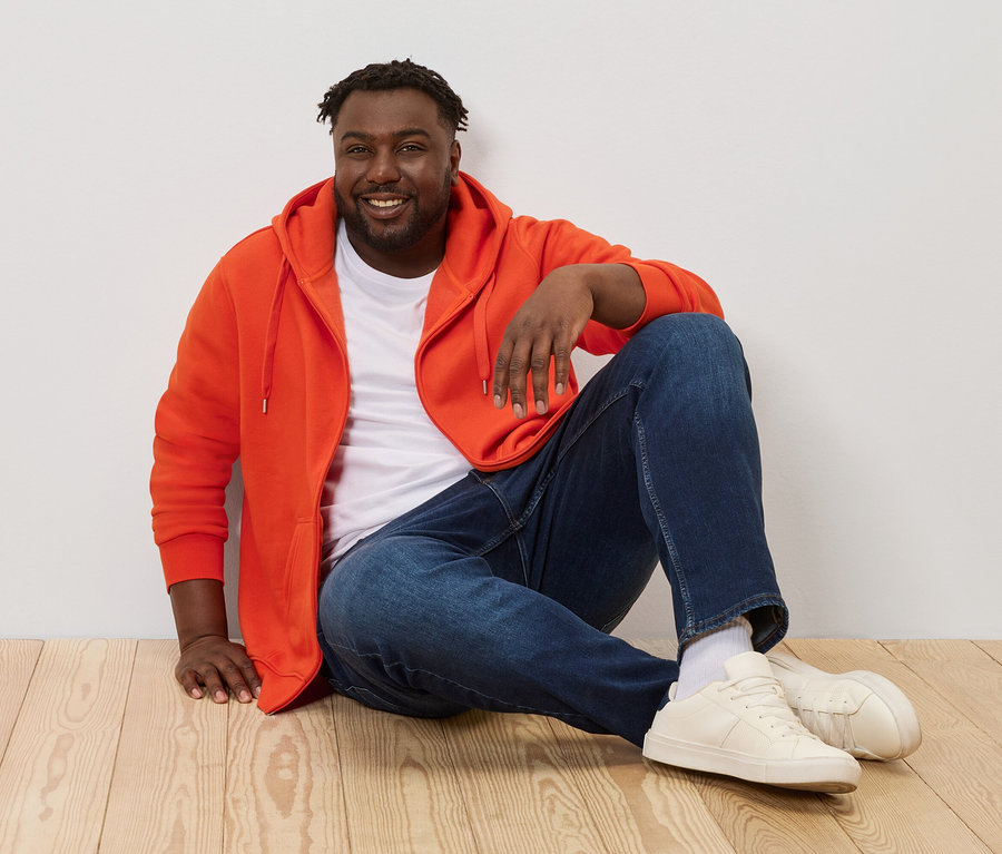 Férfi ül a fapadlón, narancssárga kapucnis felsőt visel.