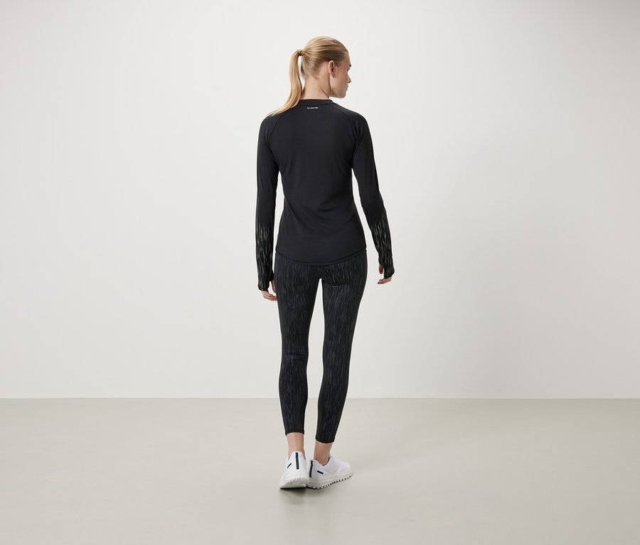 Egy nő háttal a kamerának fekete, hosszú ujjú inget és mintás leggingset visel.