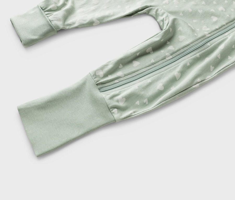 Közeli kép egy világoszöld, fehér szívmintás, cipzáras baba hálózsákról.