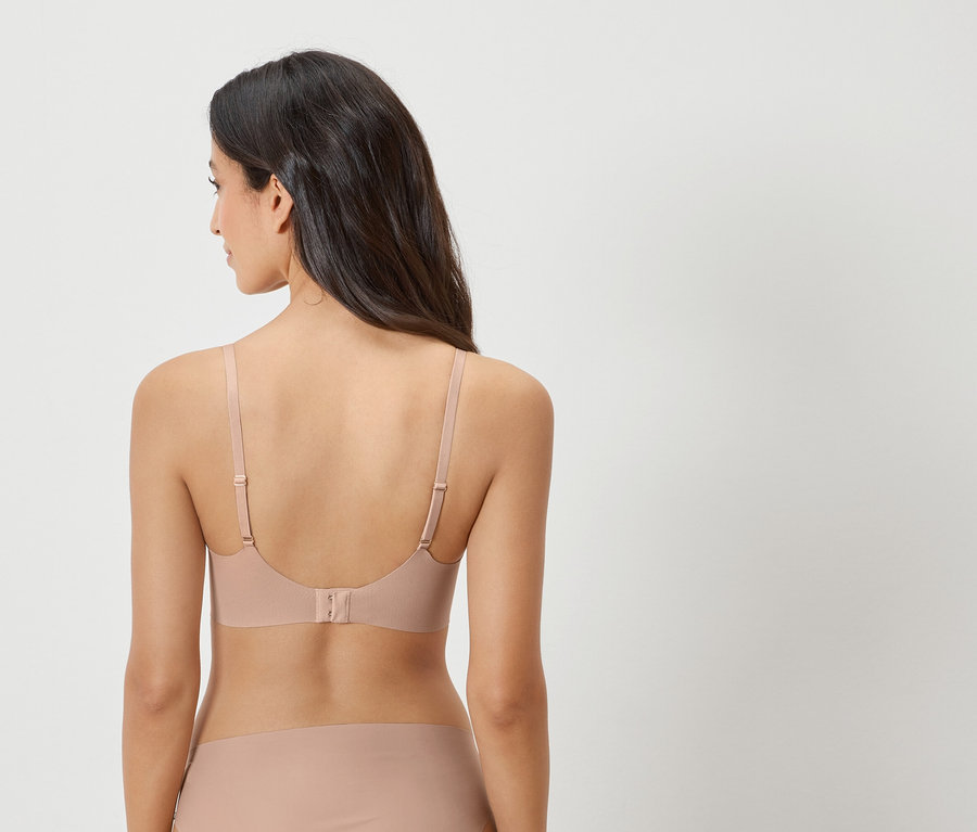 Hátulnézet egy sötét hajú nőről, aki testszínű melltartót és hozzáillő alsót visel.