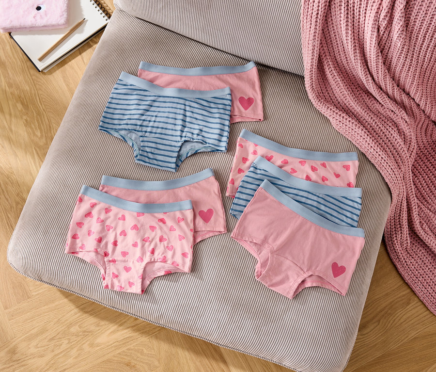 Egy csíkos párnán hat rózsaszín és kék színű lány bugyi fekszik.