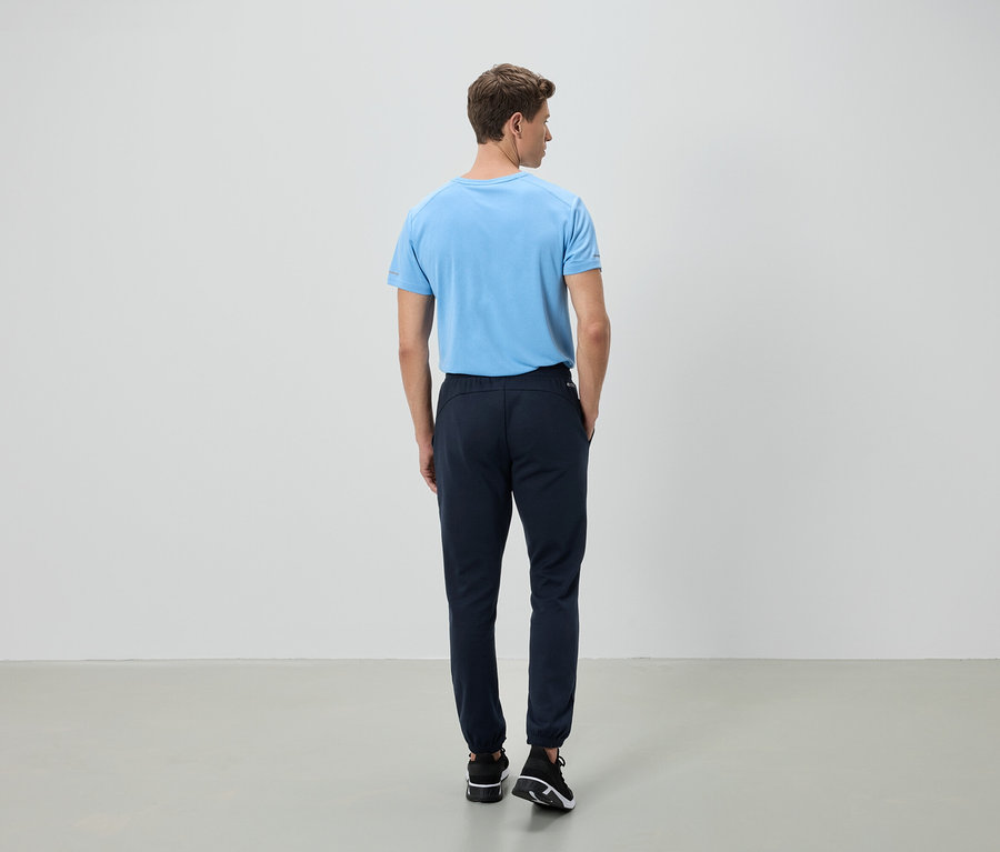 Egy férfi áll háttal a kamerának, világoskék pólót és sötétkék nadrágot visel.