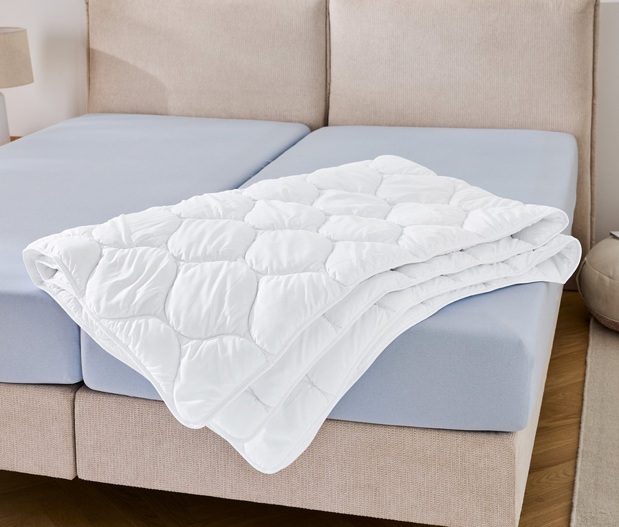 Egy nagyméretű, kifőzhető steppelt paplan összehajtva fekszik egy kék lepedőn.