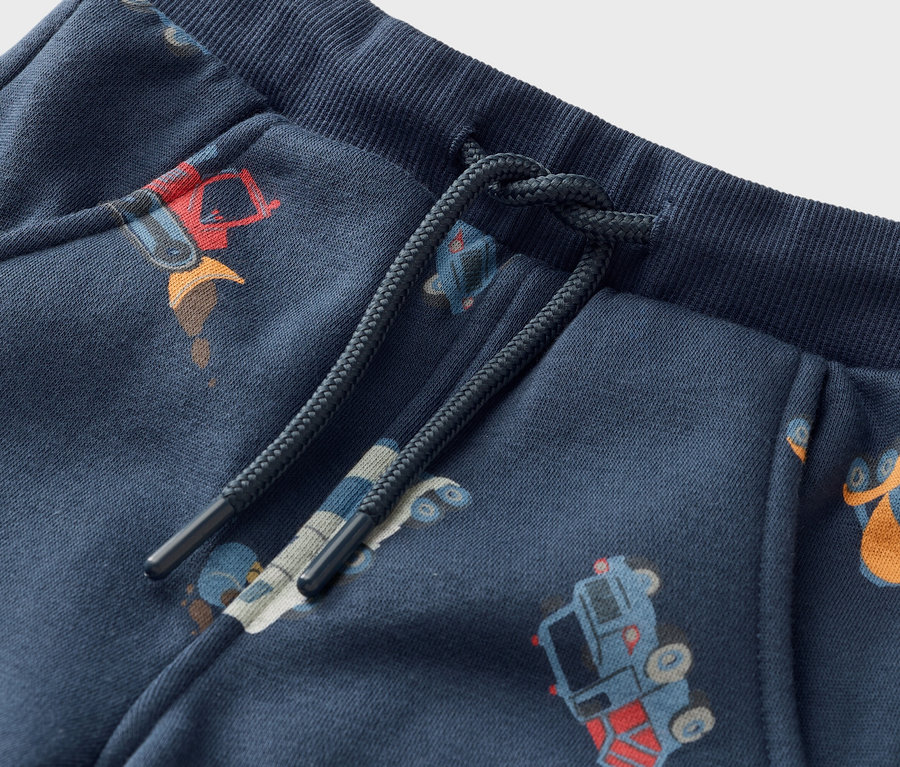 Közeli kép egy sötétkék színű, húzózsinóros, építőipari járművek mintájú jogging alsóról.