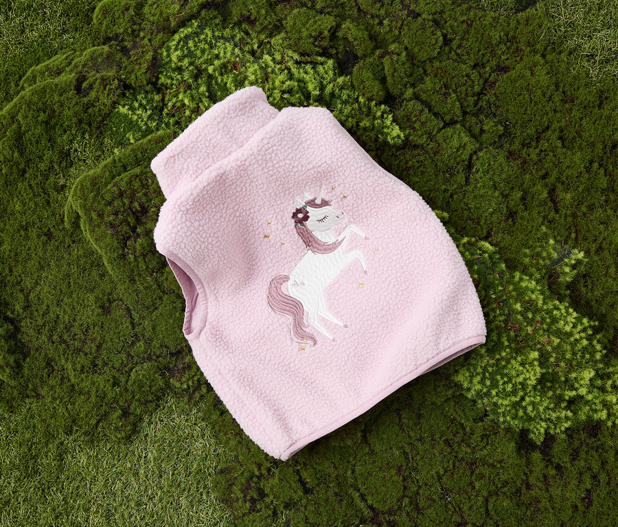 A mohán fekszik egy rózsaszín NAME IT plüssmellény gyerekeknek, unikornissal.
