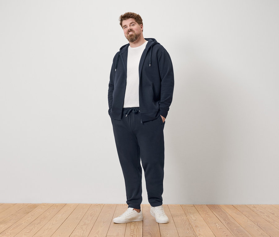 Férfi áll sötétkék tréningruhában és fehér tornacipőben.