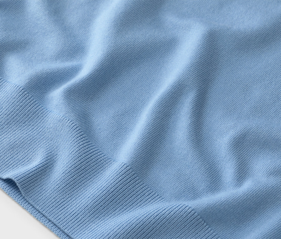 Egy világoskék kötött pulóver közeli képe bordázott mandzsettákkal.