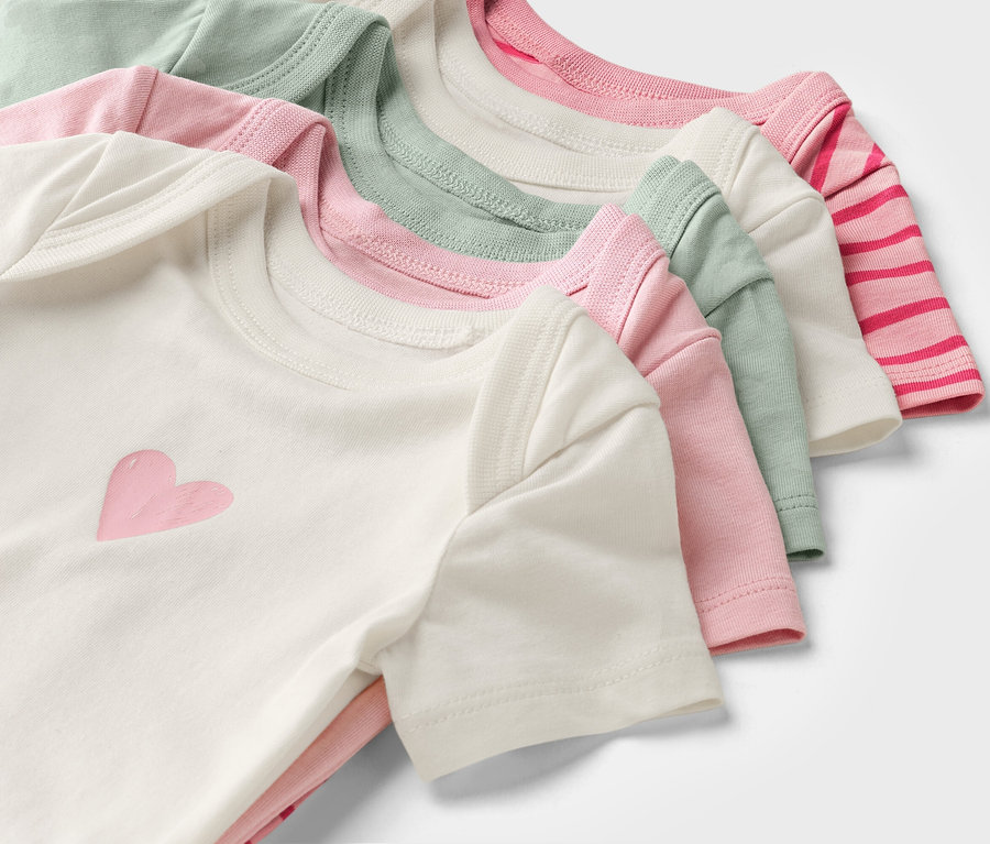Többszínű, rövid ujjú babaruhák egymásra vannak rakva.