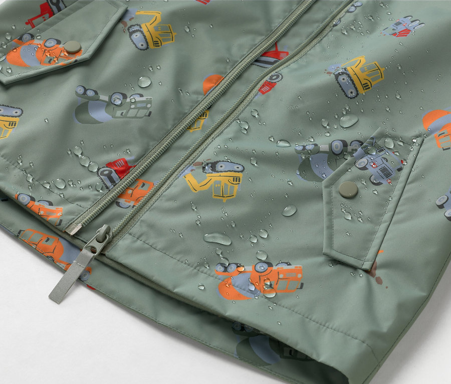 Közeli kép egy olívazöld, cipzáros, építkezés témájú kabátról, amelyet vízcseppek borítanak.