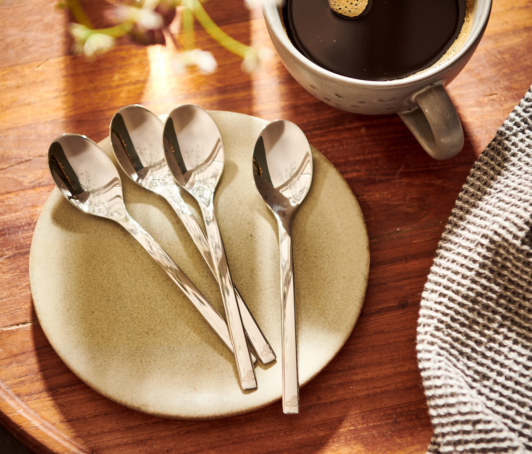 Négy kávéskanál egy tányéron egy csésze kávé mellett.