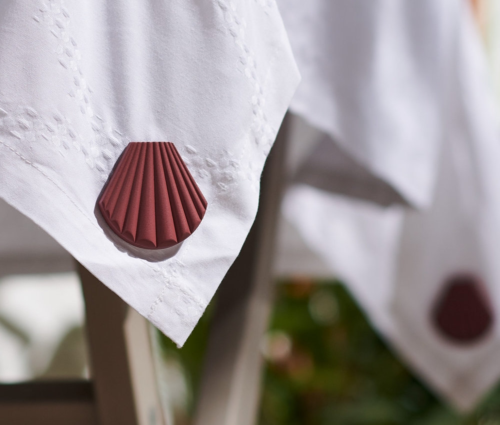 Asztal széle fehér asztalterítővel, melyet egy barna, kagyló alakú, 4 mágneses asztalterítő-leszorító szettben rögzítettek.