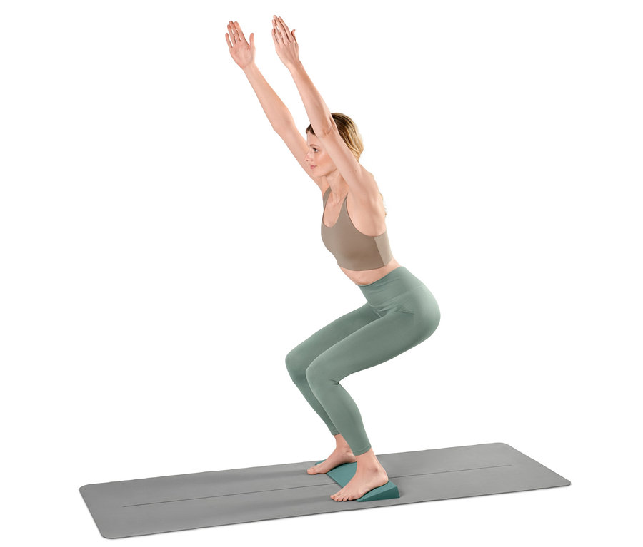 Nő széktartást végez jógaszőnyegen, a sarkai alatt egy jógaékkel.