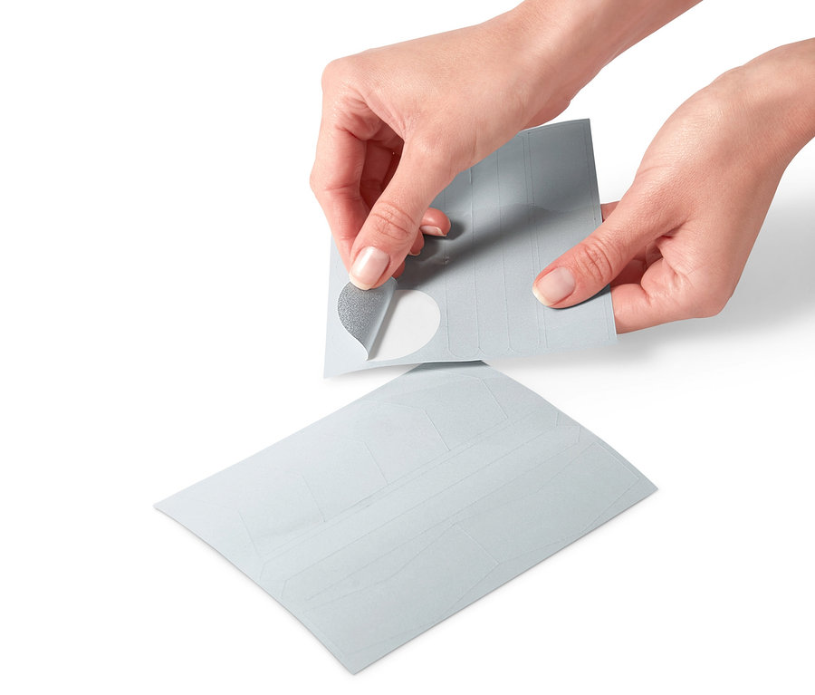 Kezek húznak le egy fényvisszaverő matricát egy 16 darabos fényvisszaverő matricakészlet ívéről.