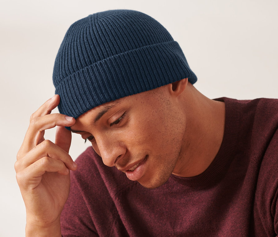 Egy férfi a homlokához ér, és egy sötétkék kötött sapkát visel.