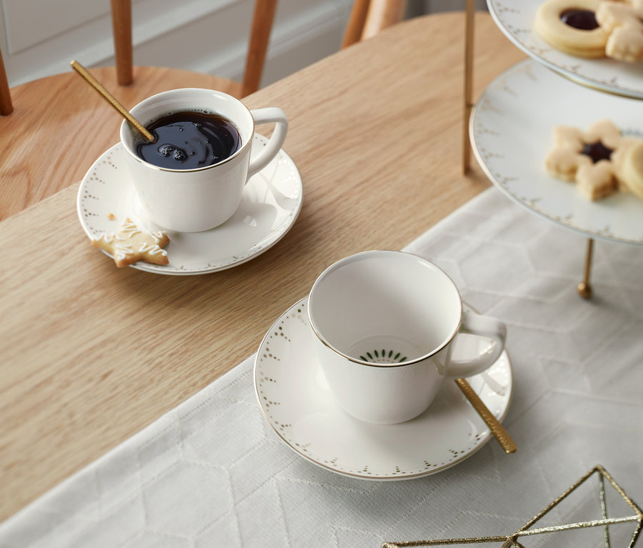 Az asztalon egy 2 darabos, arany mintás porcelán kávéscsésze, egy csésze kávéval és egy keksszel.