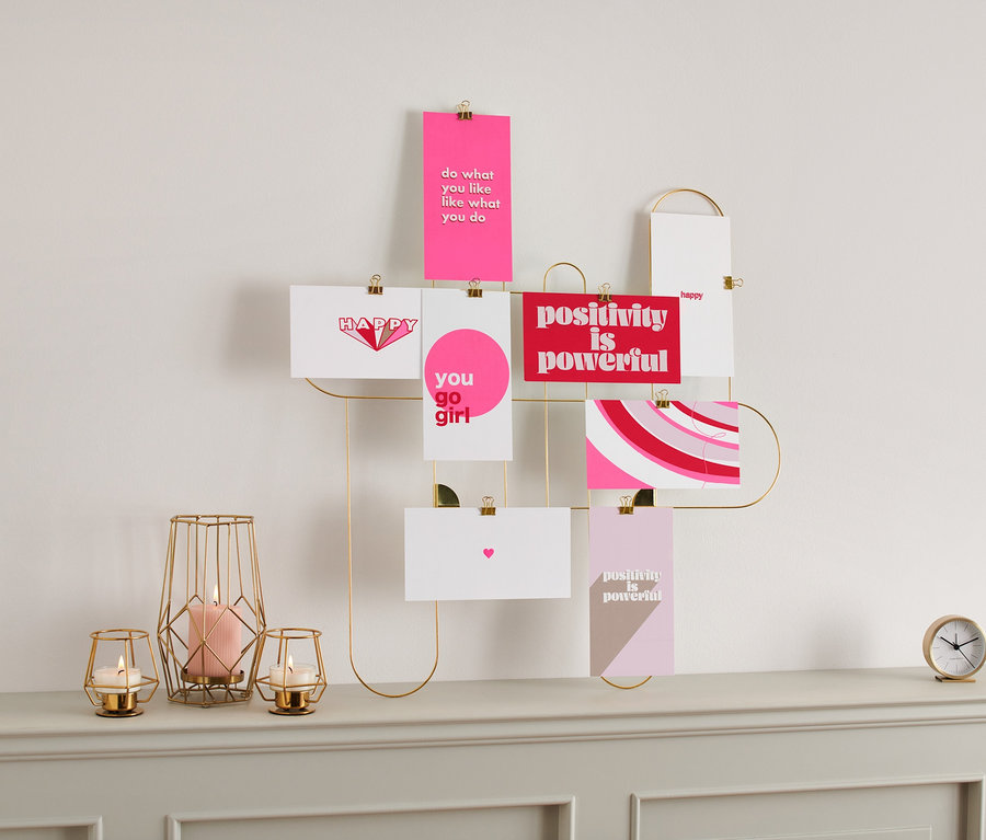 Egy aranyszínű kereten képeslapok és mini képek lógnak a falon. Gyertyák és óra állnak a komódon.