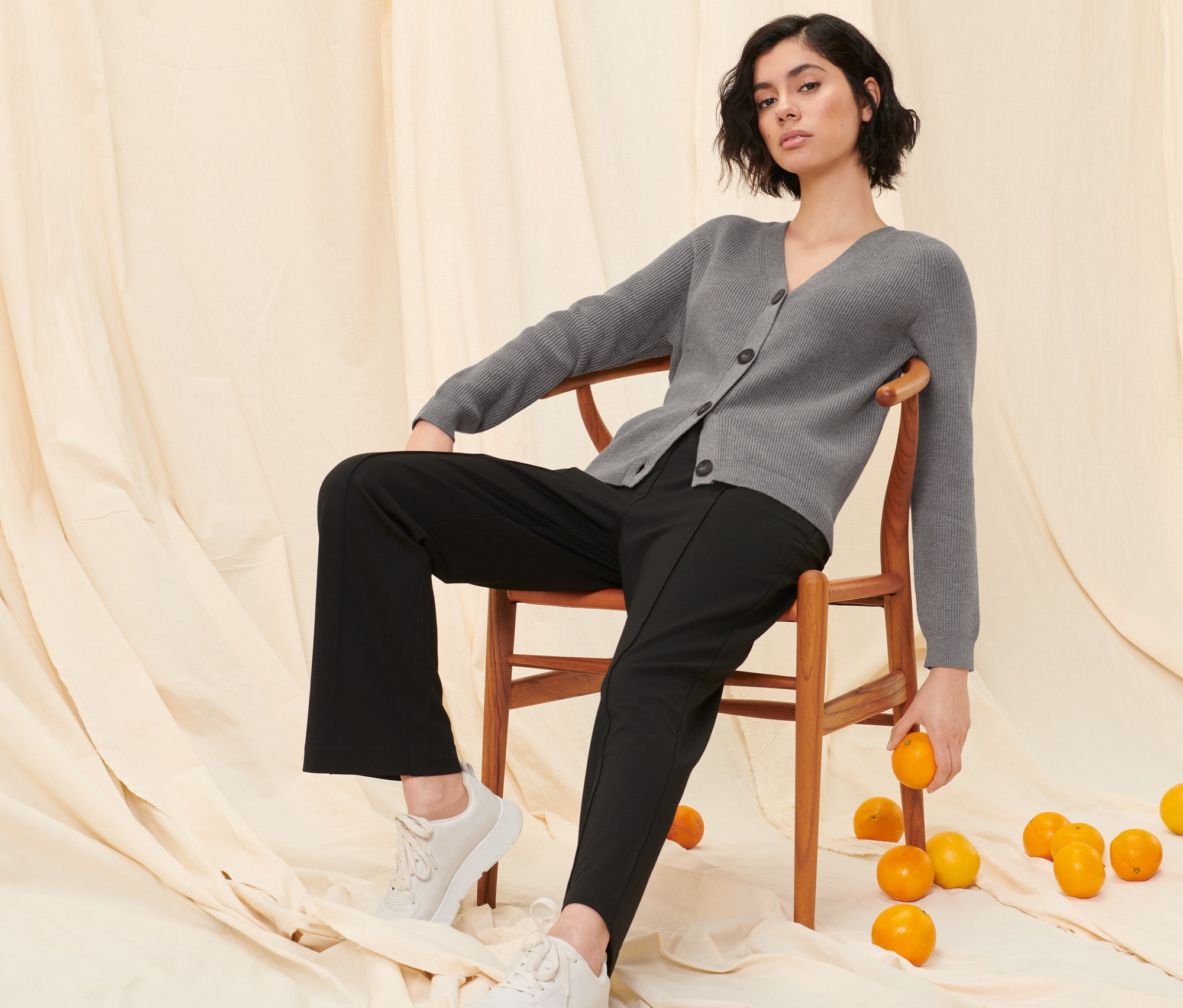 Nő ül egy széken szürke kötött kardigánban és fekete szabadidőnadrágban.