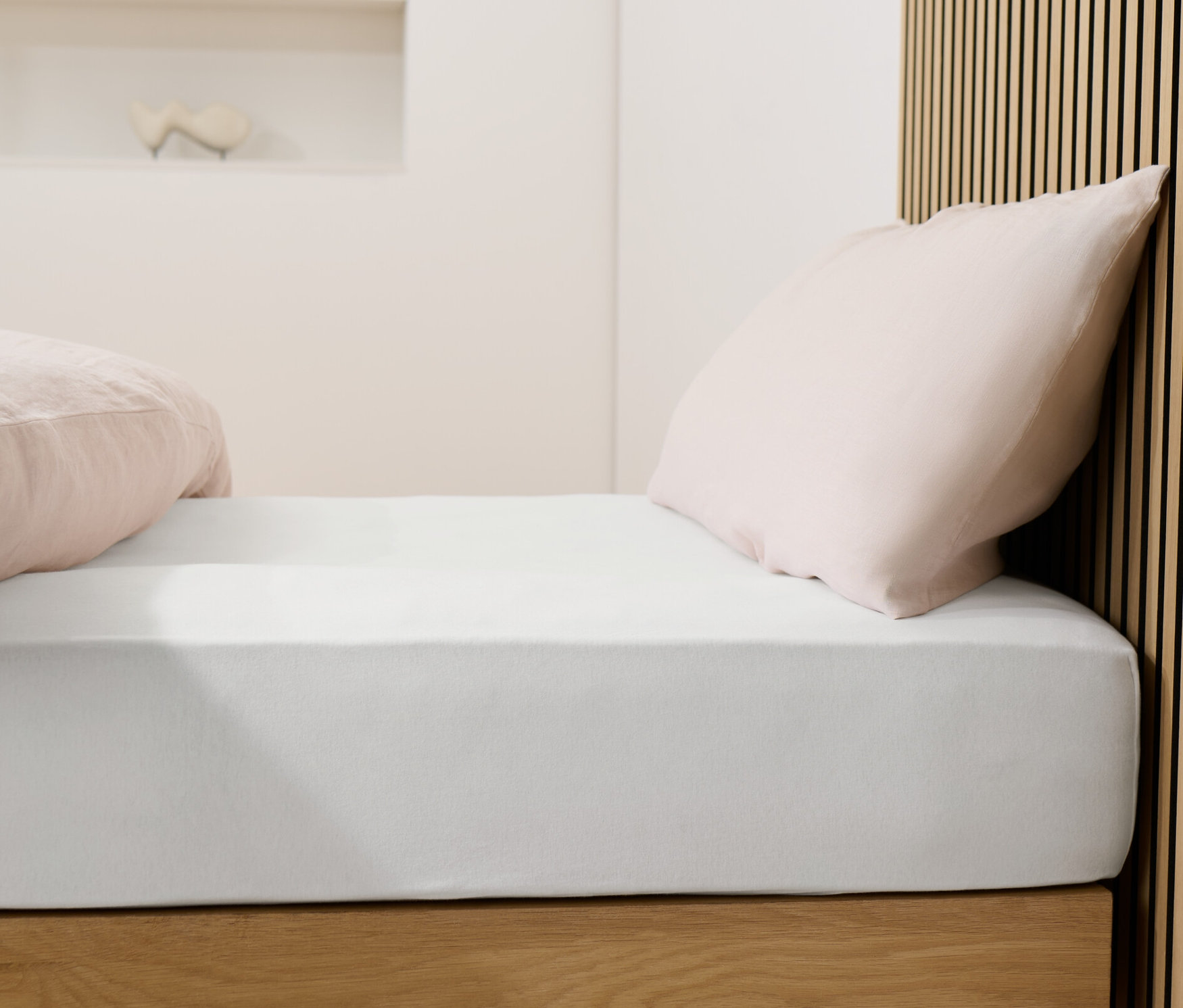 Ágy fehér jersey lepedővel és rózsaszín párnákkal.