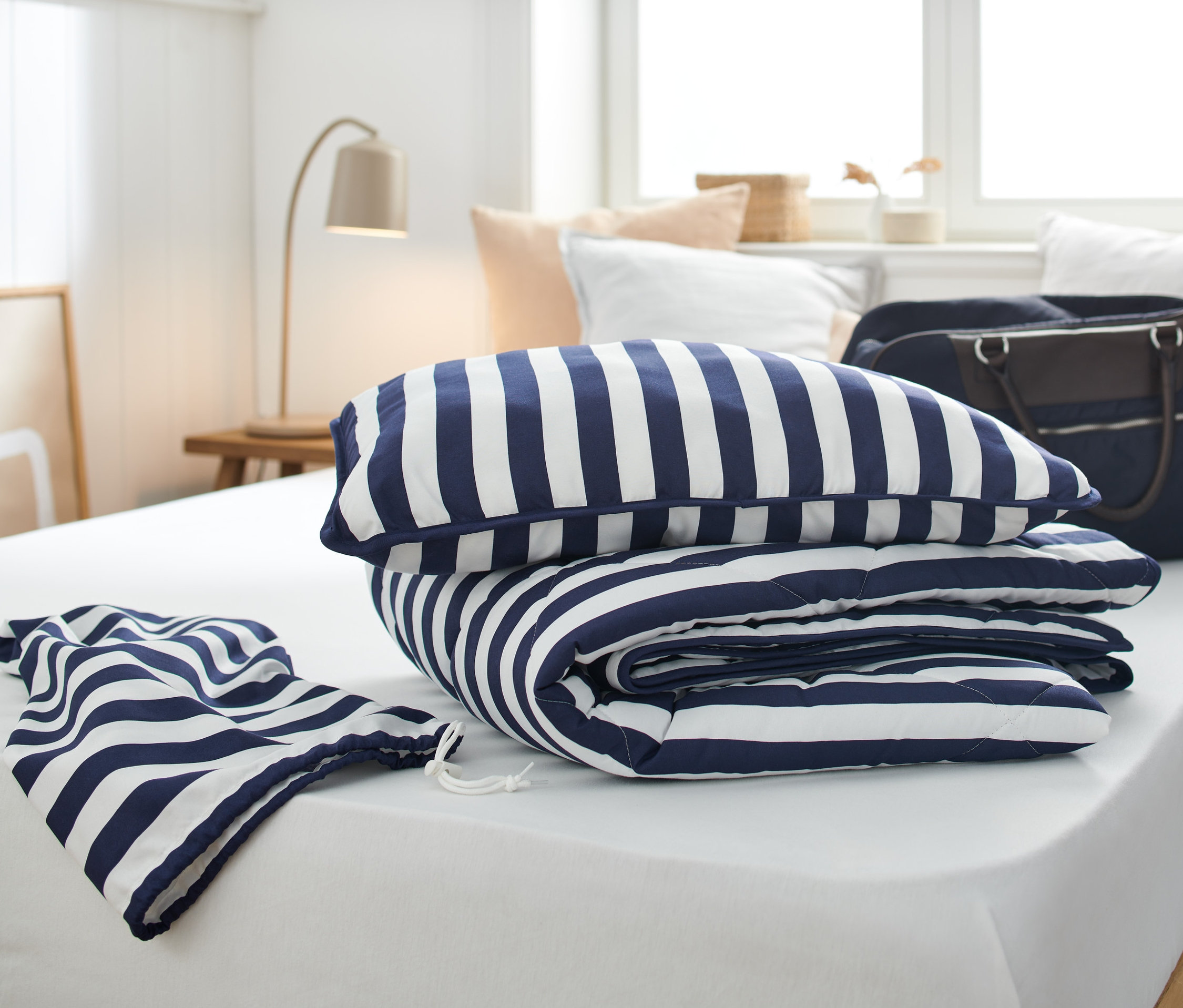Egy kék-fehér csíkos ágyneműgarnitúra utazáshoz van egy fehér ágyon.