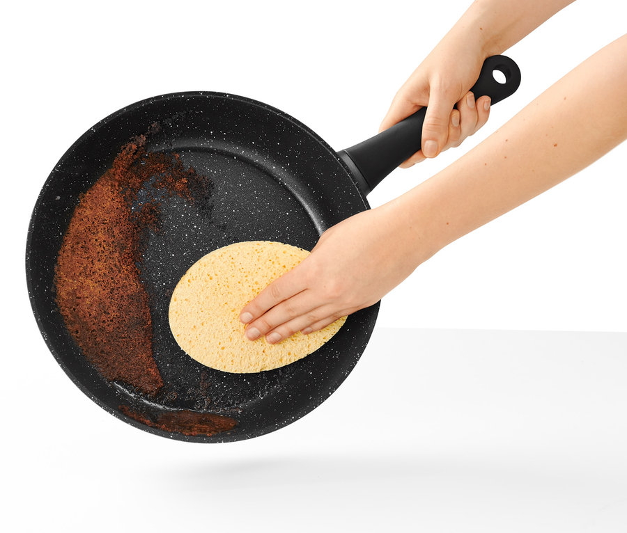 Egy 28 cm-es, kőhatású profi serpenyőt tisztítanak szivaccsal.