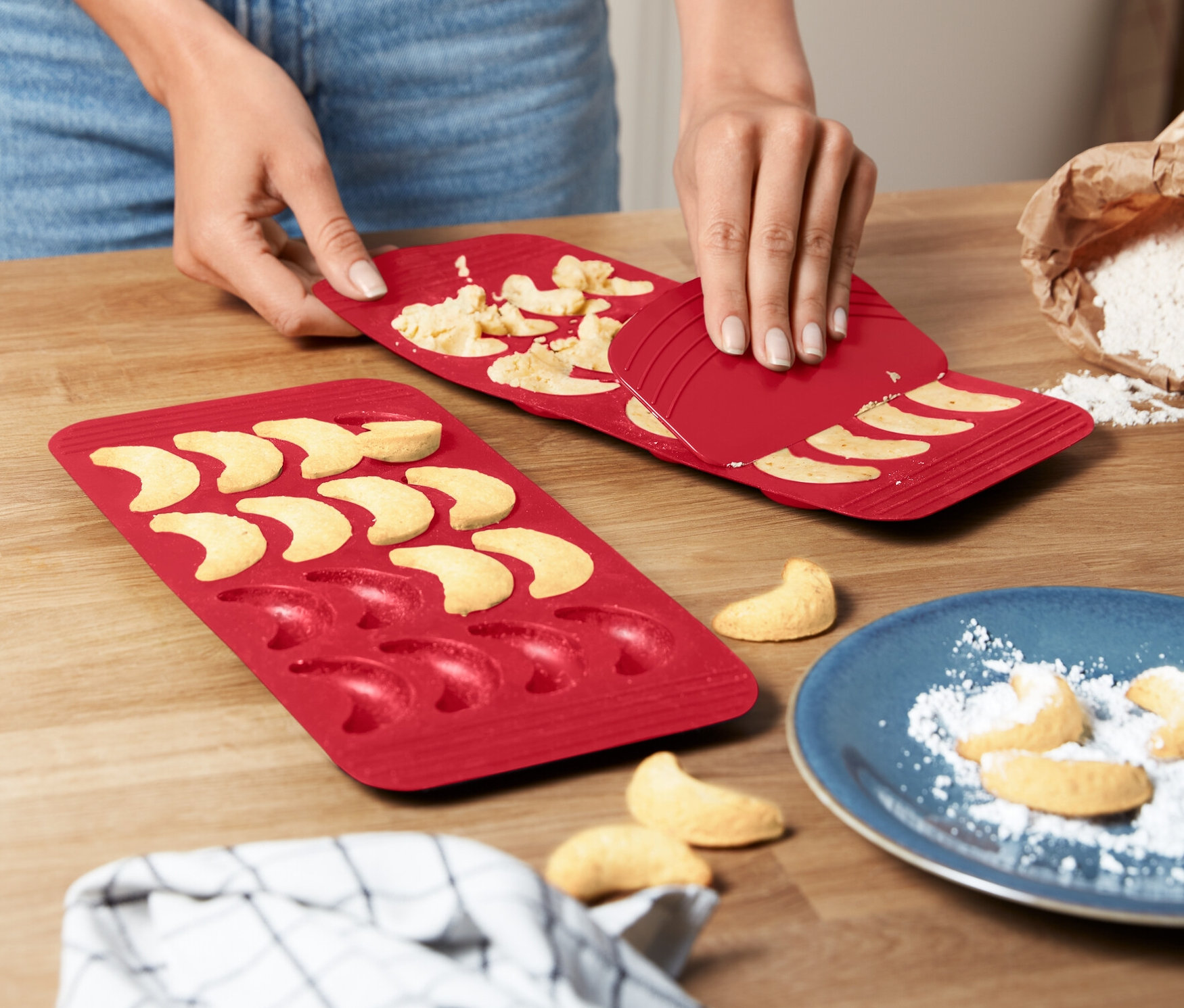 Egy nő vaníliás kifliket vesz ki egy piros 2 szilikon vaníliás kifli sütőformából.