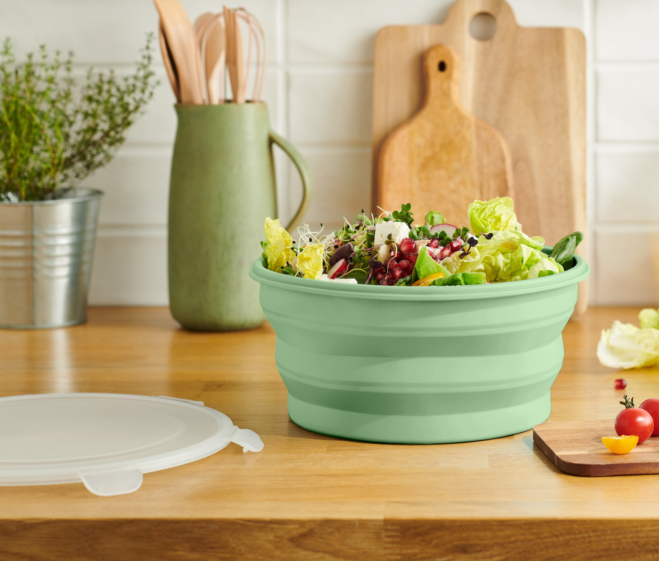 Egy zöld, összehajtható salátástál tele salátával egy fa konyhapulton áll.
