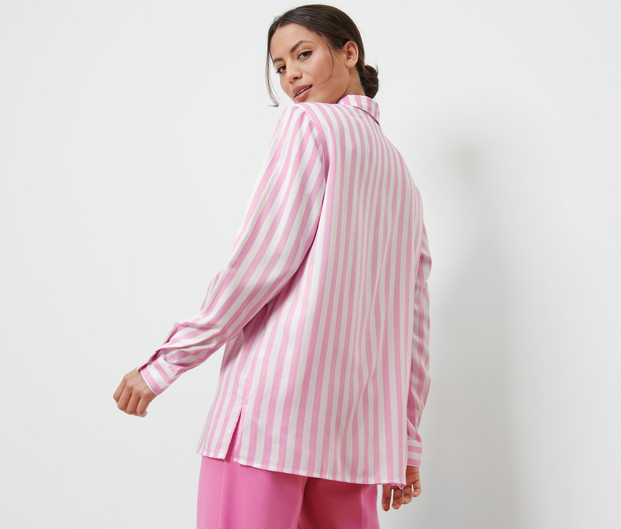 Egy nő a válla fölött hátra néz, rózsaszín csíkos blúzt visel.