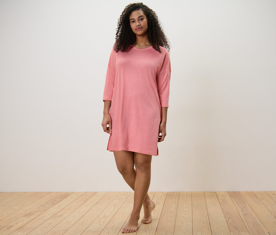 Egy nő áll mezítláb, korall színű hálóingben.