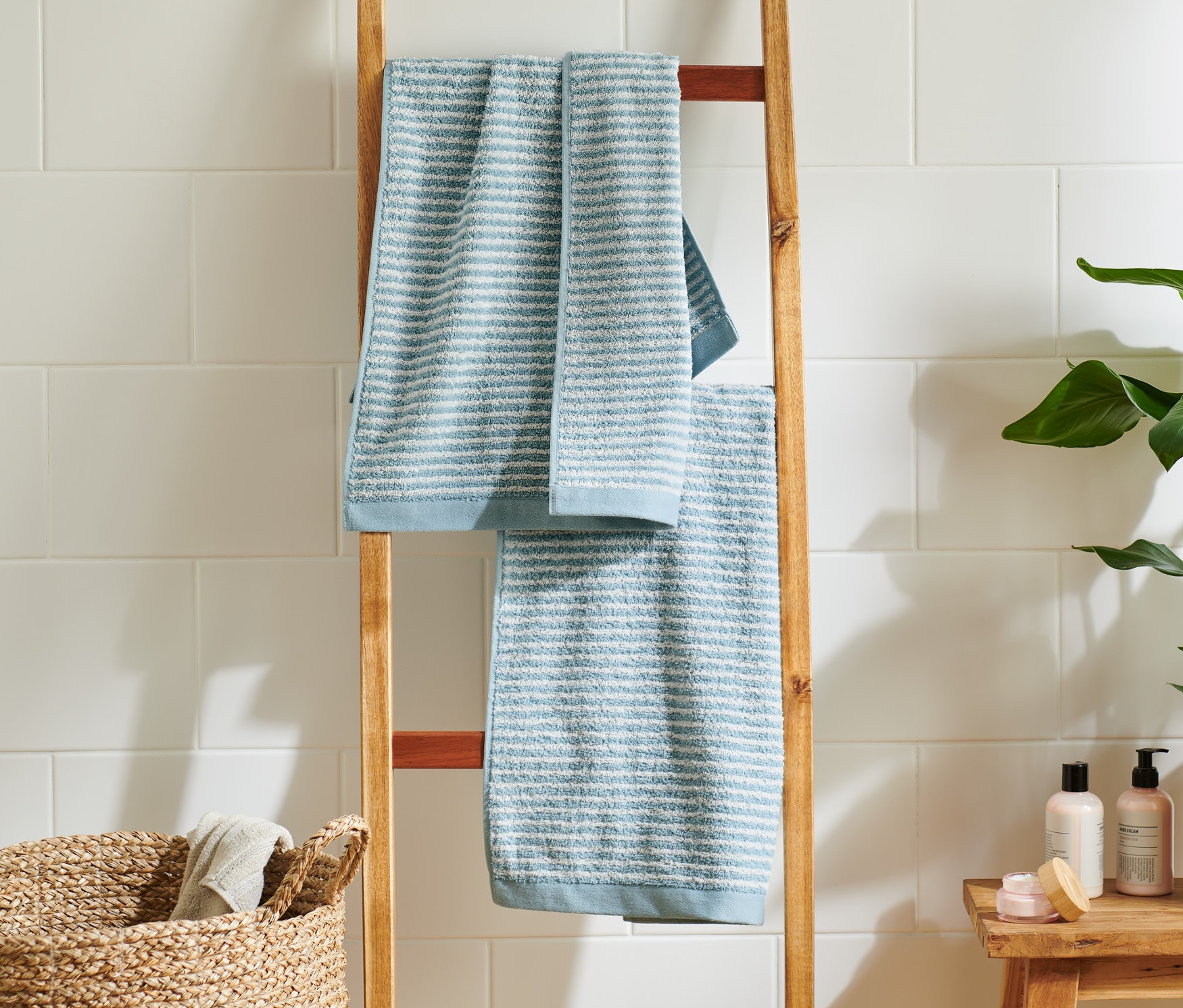 Két kiváló minőségű világoskék és kék törölköző lóg egy fa létrán a fürdőszobában.