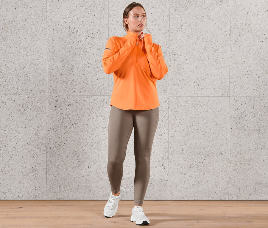 Nő visel neonnarancssárga funkcionális termofelsőt és sportnadrágot.