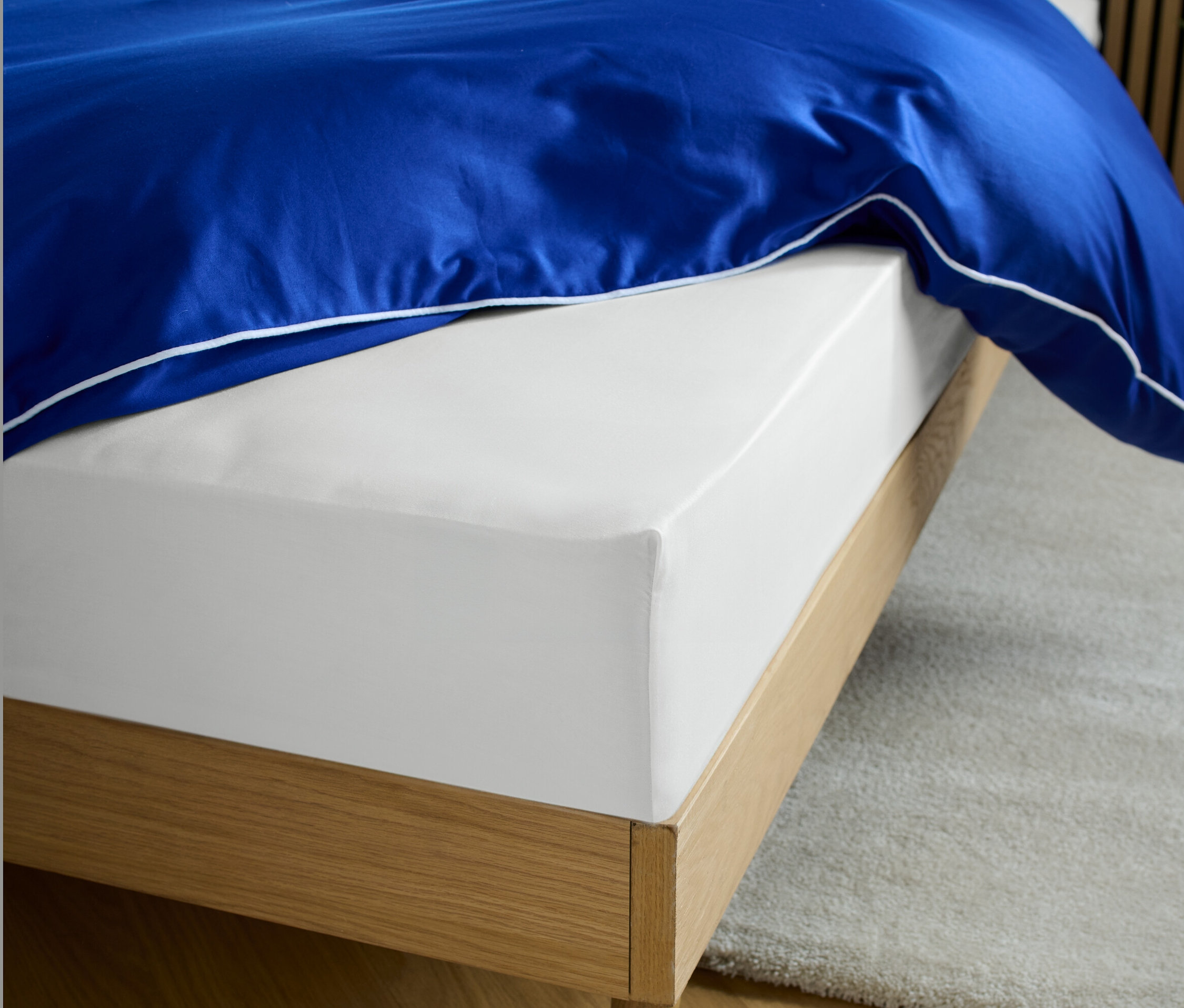 Egy fehér szatén gumis lepedő egy ágyon, kék paplannal.