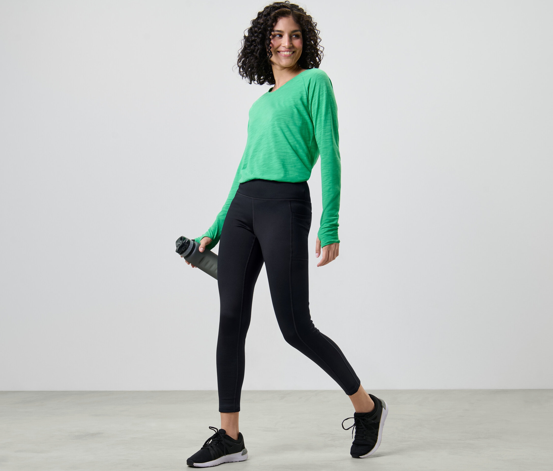 Nő zöld felsőben és fekete női funkcionális termonadrágban vizet tart.