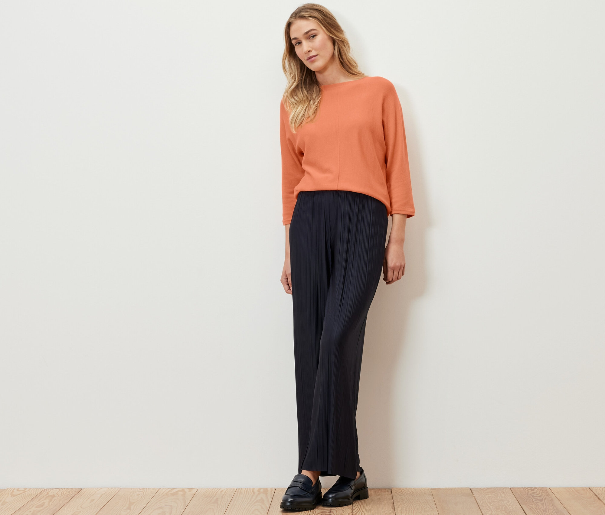 Nő áll, és barack színű, finomkötésű merinópulóvert visel.