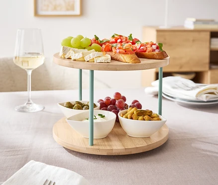 Egy forgó kínáló tálca áll az asztalon, rajta bruschetta, sajt és gyümölcsök.
