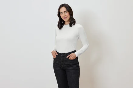 Nő kezével a sötét farmernadrág zsebében és fehér, hosszú ujjú pólóban.