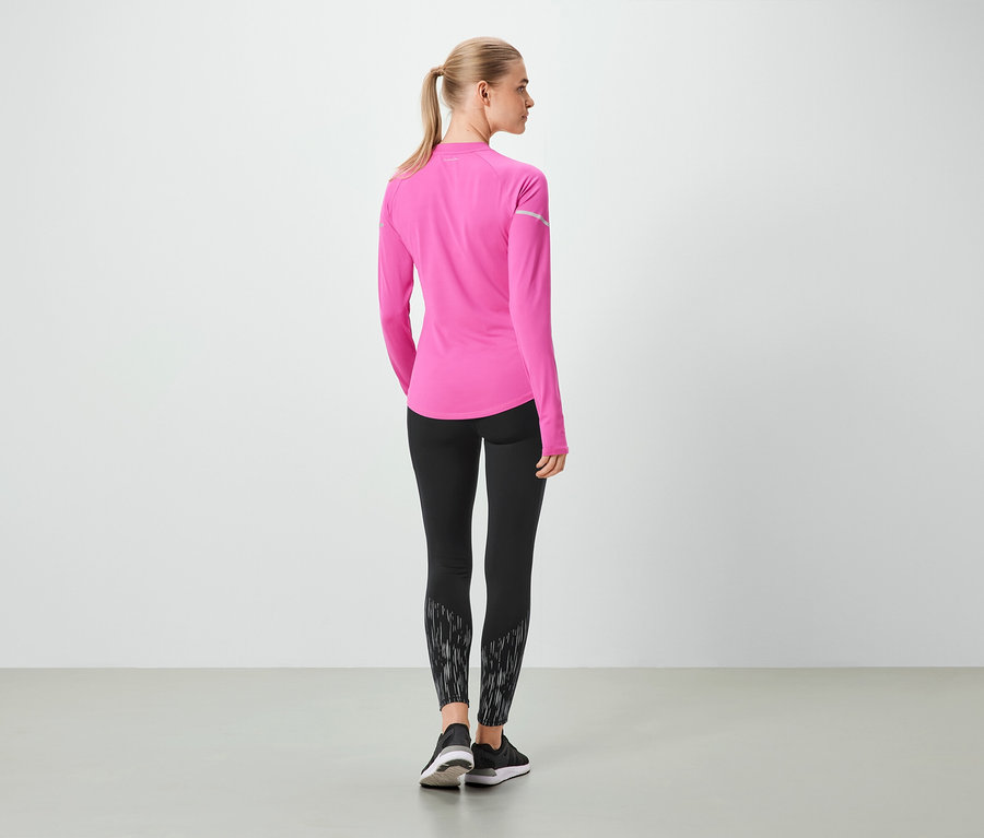 Egy nő háttal a kamerának rózsaszín, hosszú ujjú felsőt és fekete leggingst visel.