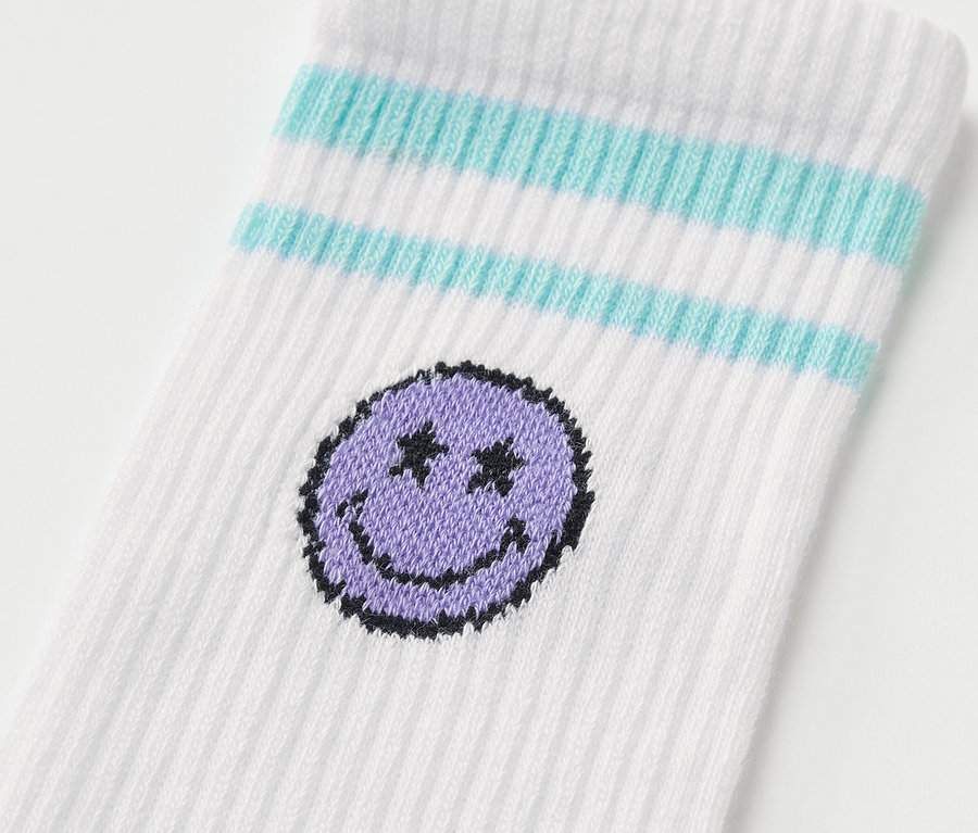 Egy fehér zokni részlete kék csíkokkal és lila mosolygós fejjel. 5 pár SMILEYWORLD® gyerek sportzokni.