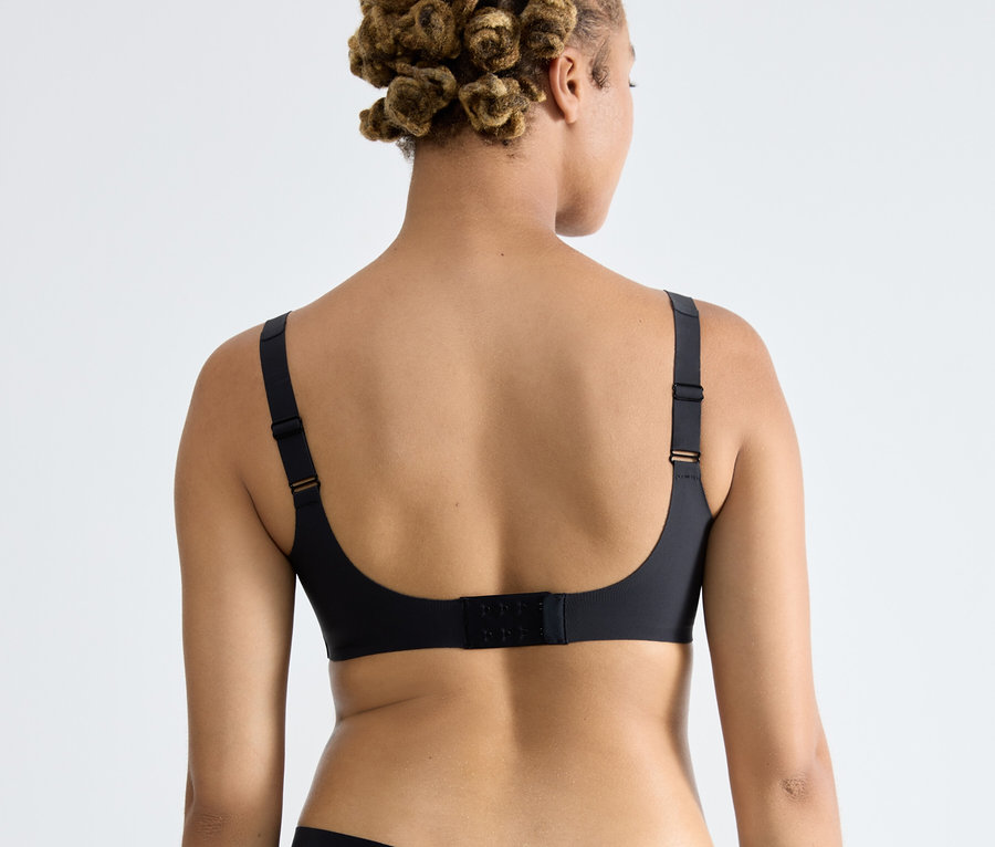 Hátulról látható egy afro frizurás nő, aki fekete sloggi ZERO Feel 2.0 puha melltartót visel.