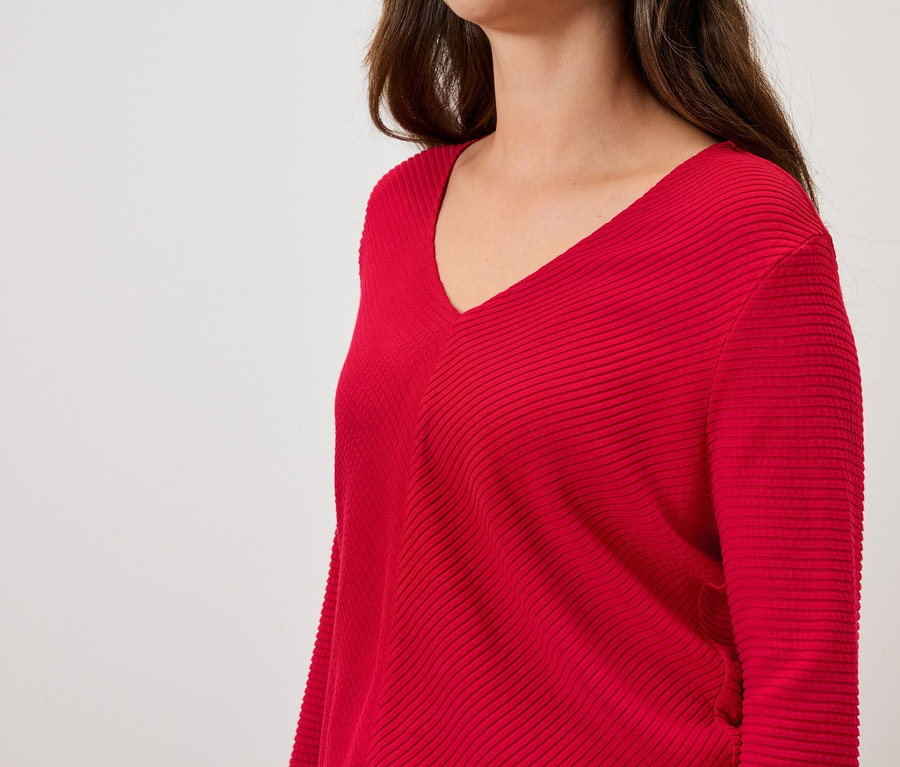 Nő visel egy piros, hosszú ujjú, V-nyakú pulóvert.