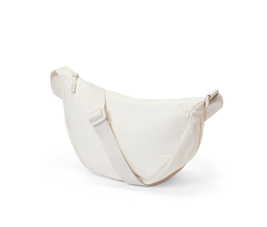 Egy krémszínű oldaltáska fekszik egy fehér háttéren.
