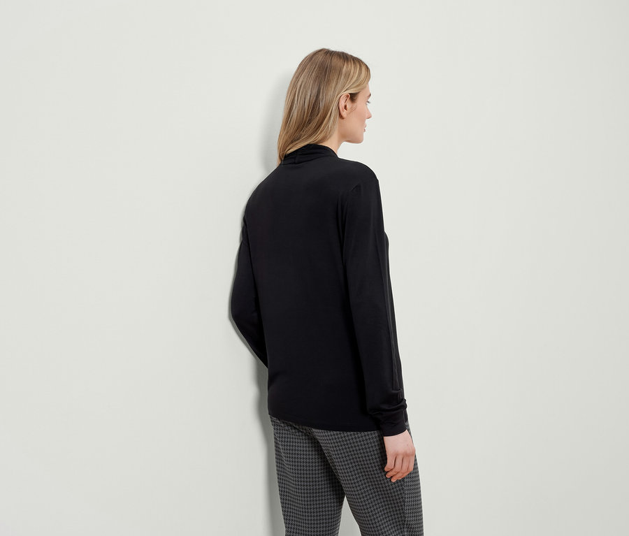 Egy hátulról látható nő fekete, hosszú ujjú felsőt és tyúkláb mintás nadrágot visel.