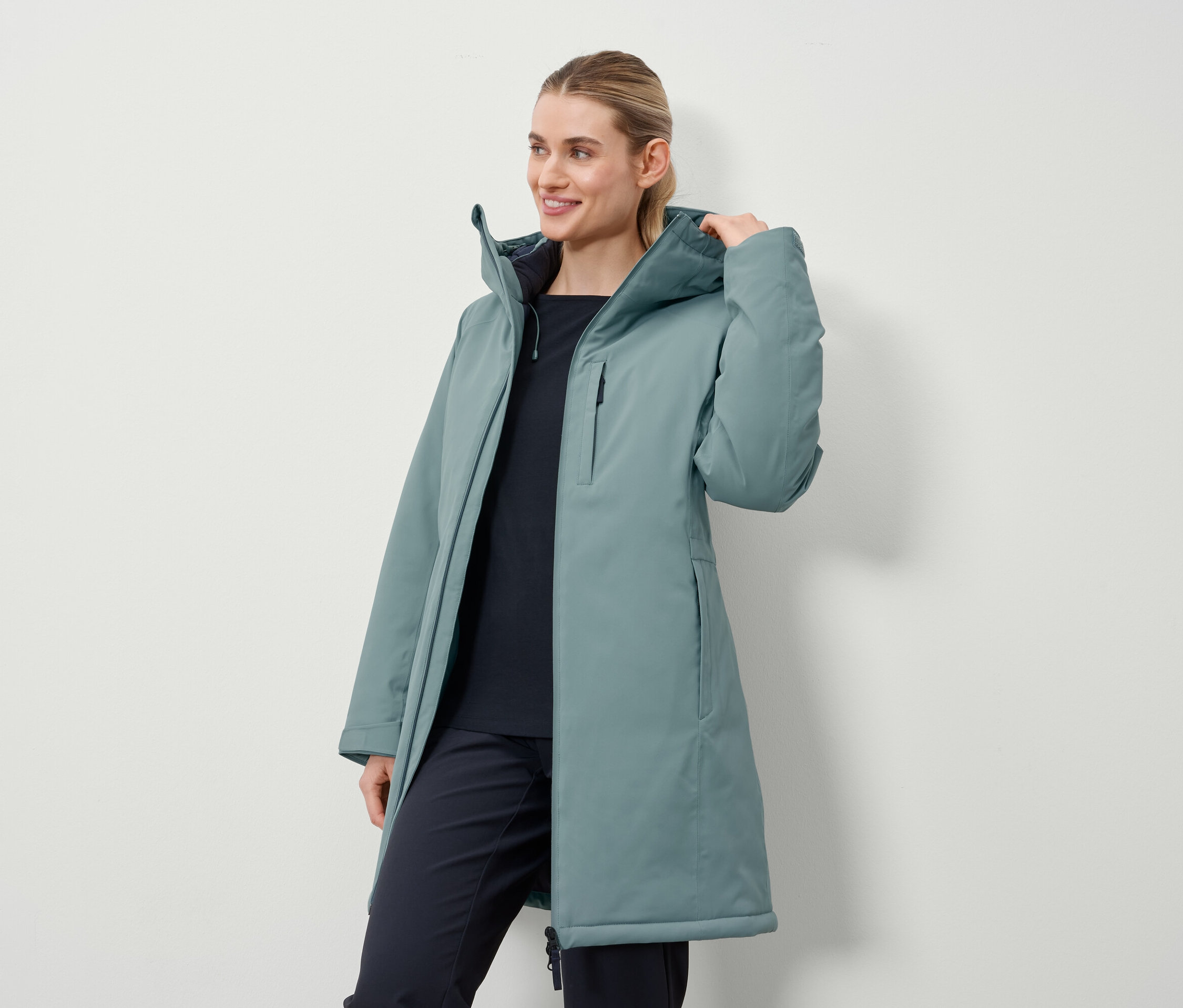 Egy nő petróleum színű, hosszú kabátot visel.