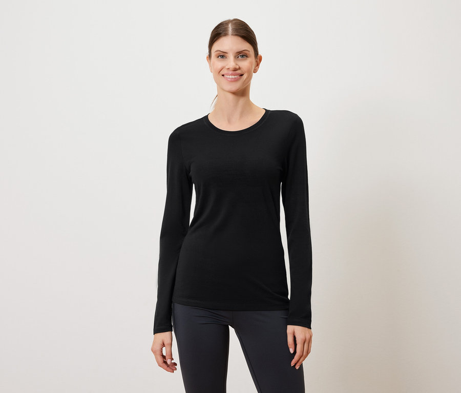 Nő visel fekete hosszú ujjú inget és sötét leggingst fehér háttér előtt.