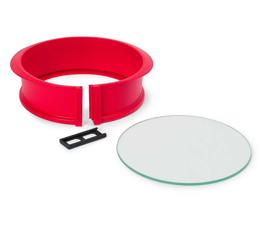 Piros, kerek tortaforma fekete csíptetővel és kerek üveglappal fehér háttér előtt.