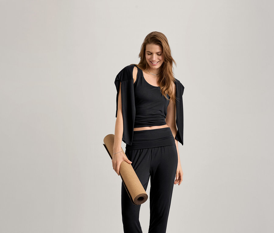 Nő jógamatracot tart és fekete, női 2 az 1-ben sportfelsőt visel.